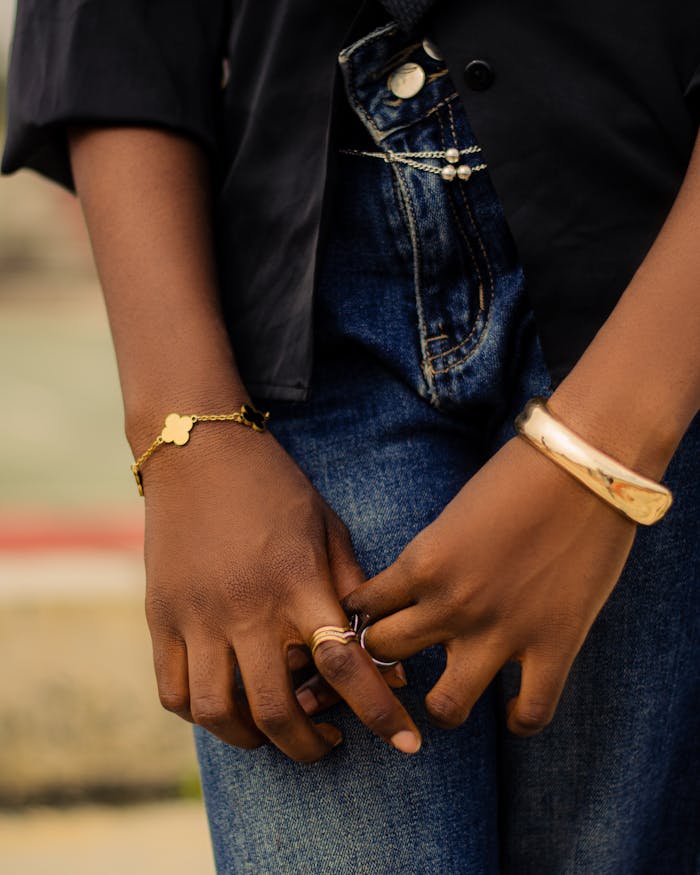 Close-up of hands with elegant bracelets and rings, denim jeans in background.